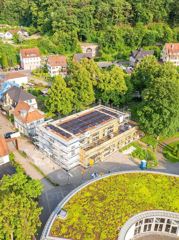 Aerial view of a construction site in a residential area surrounded by trees and green roofs on a summer's day, Hirsau, Calw, Germany