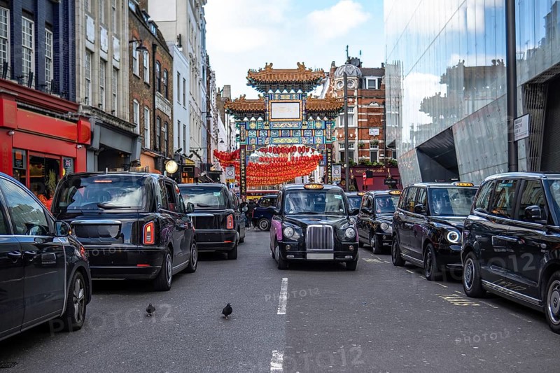 Black cabs are waiting in traffic under a decorated paifang, a traditional chinese architectural arch or gateway structure, in london chinatown