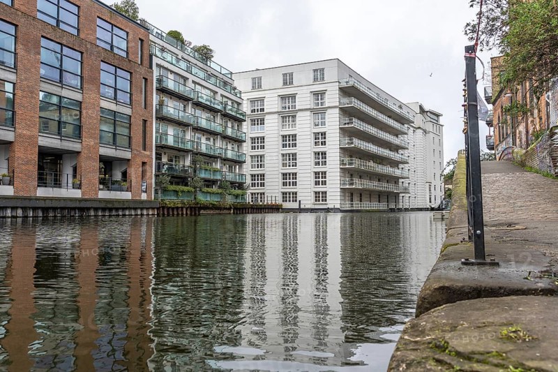 Modern and historic buildings reflecting in the calm waters of regent's canal in the city of london on a cloudy day