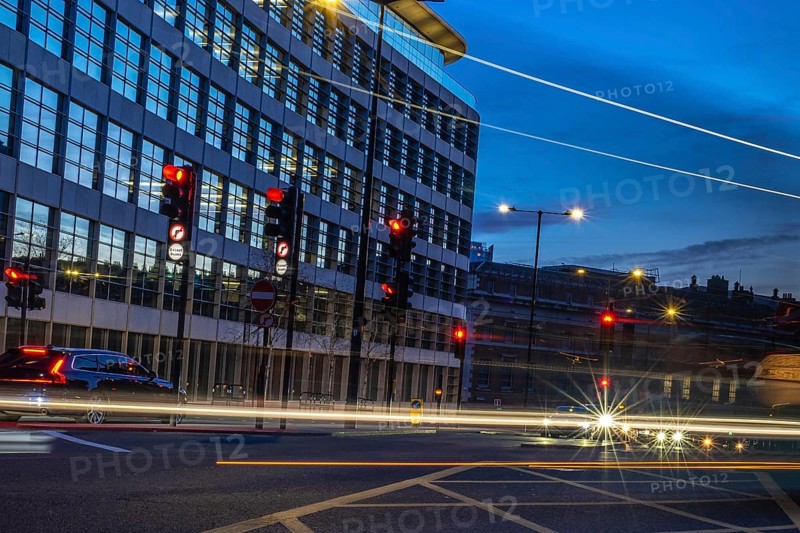 Cars passing by on a london street at dusk, with traffic lights turning red and offices in the background