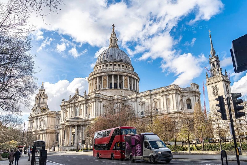 Red double decker bus driving on a street next to st paul's cathedral in london, uk, on a sunny spring day