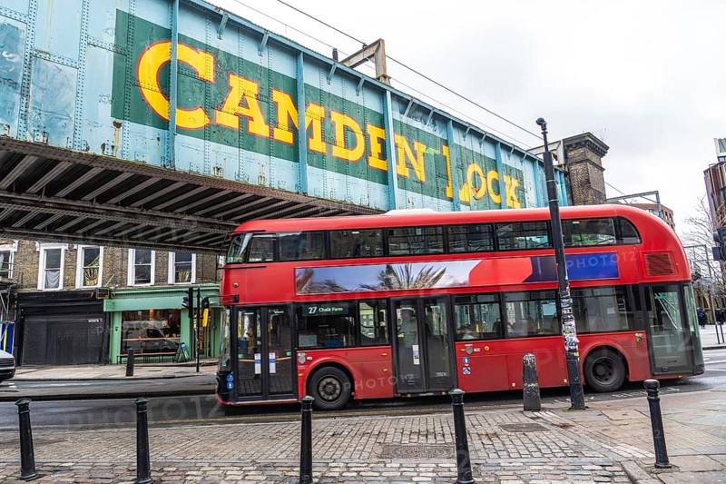 Iconic red double decker bus driving through camden town in london, under the bridge with the camden lock writing