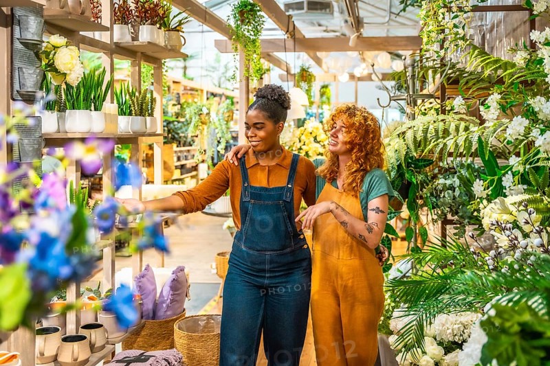 Two young women working together in a garden center, discussing vibrant plants and creative flower arrangements while enjoying their teamwork