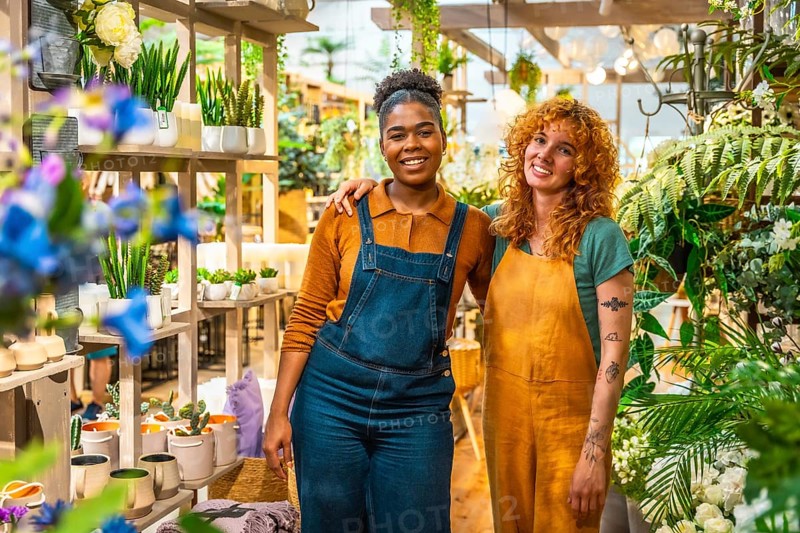 Two joyful florists posing together in their vibrant flower shop, surrounded by a colorful array of plants and beautiful blooms