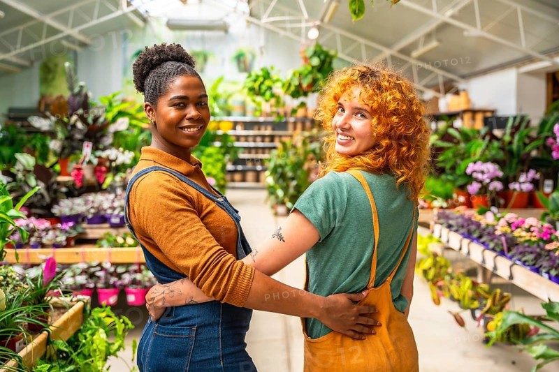 Two happy florists are hugging each other, smiling, while working in their plant nursery greenhouse