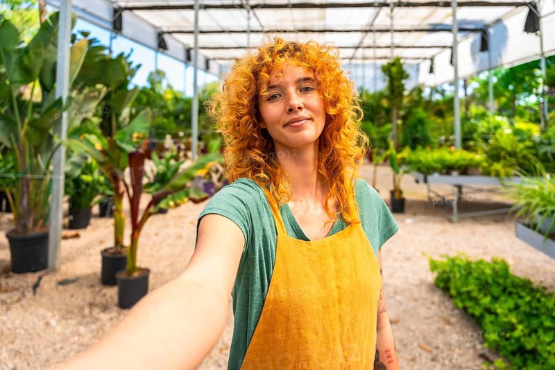Confident red haired female gardener taking a selfie in a greenhouse, showcasing her passion for plants and sustainable living