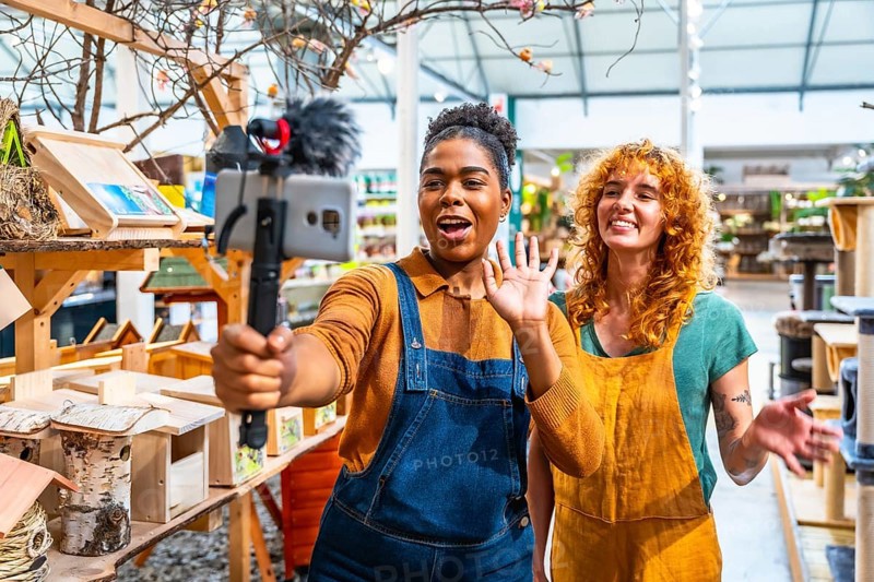 Two happy saleswomen waving at the camera while filming a video for social media marketing in a pet shop