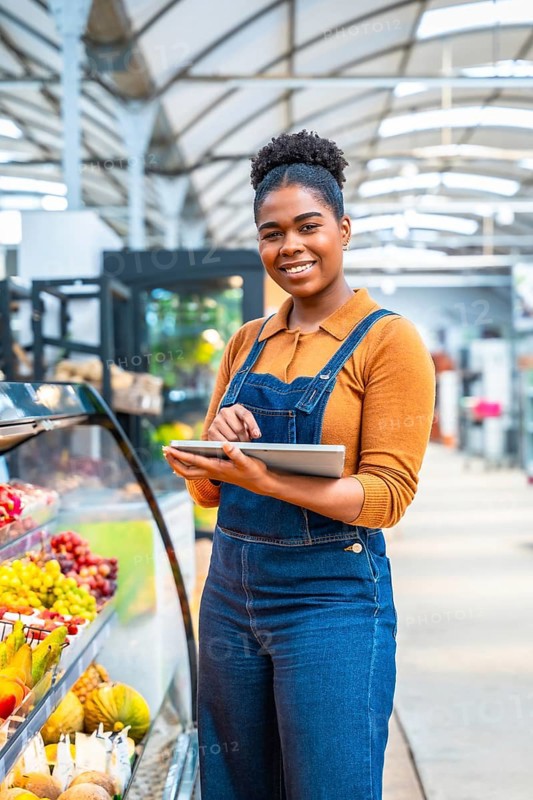 Young supermarket employee managing fresh fruit section inventory using a digital tablet, ensuring quality and availability for customers