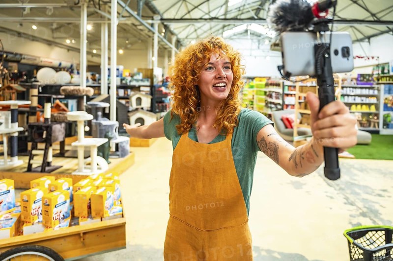 Young saleswoman filming a video for social media with a smartphone and microphone, showing pet products in a pet shop