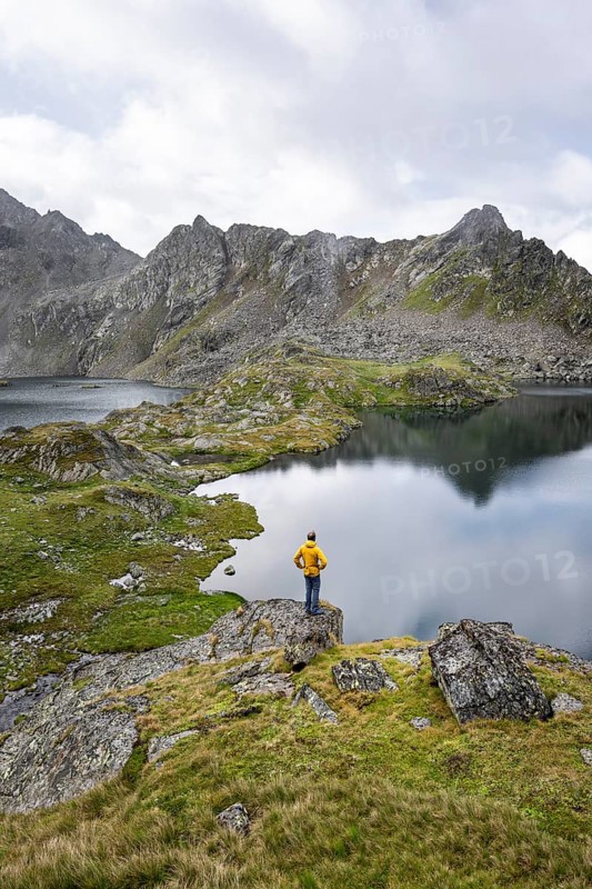 Mountaineer on a rock in front of mountain lakes Wangenitzsee and Kreuzsee, cloudy mountain peaks in the morning, Schober group, Hohe Tauern National Park, Carinthia, Austria