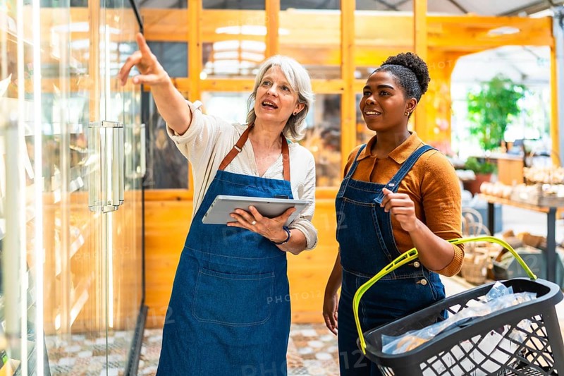 Two supermarket workers using digital tablet and basket, managing inventory and ensuring efficient restocking in a busy supermarket environment