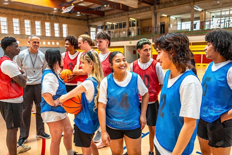 High school basketball team listening to their coach's instructions during a training session in the gym