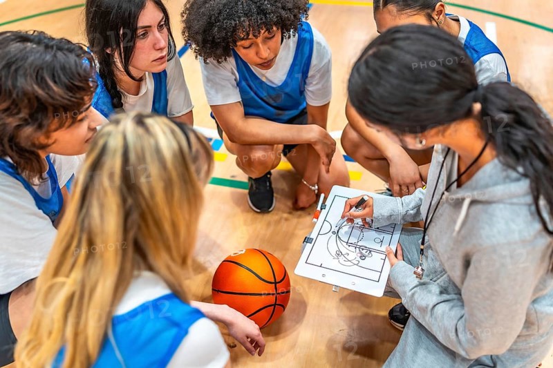 Female basketball coach drawing a play on a whiteboard and explaining game strategy to her young multi ethnic team during a time out