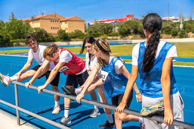 Runners stretching their legs on a vibrant blue track, preparing for a race while enjoying the summer sun and outdoor atmosphere