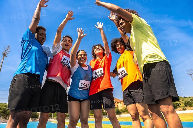 Group of young runners celebrating their victory with arms raised high after crossing the finish line on a vibrant running track