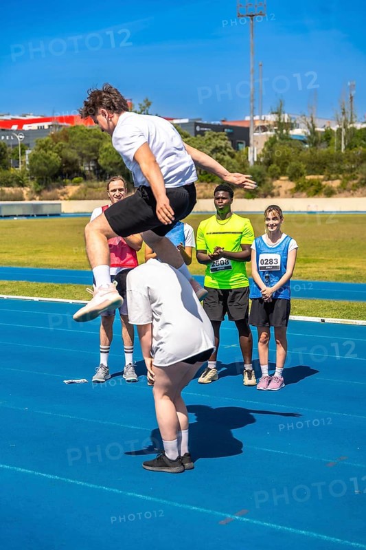 Young athlete jumps over a teammate on a track, showcasing teamwork and athleticism during a track and field competition