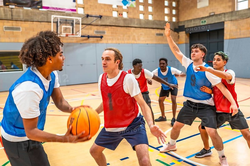 Group of young basketball players engaging in an intense match within a gymnasium, showcasing teamwork and athletic skills on the court