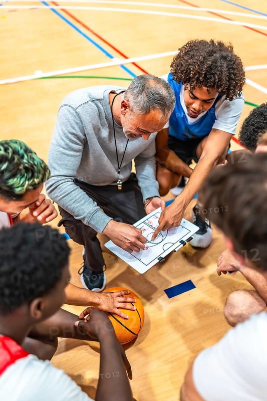 Basketball coach discussing game strategy with team players during a timeout on the court, fostering teamwork and tactical understanding