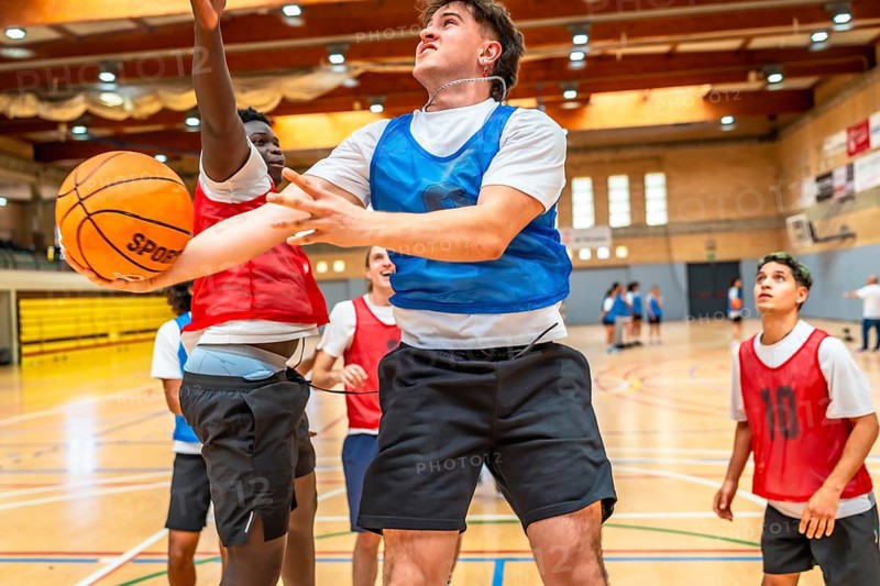 Two basketball players jumping for a rebound during a fast paced indoor court game, showcasing athleticism and competition