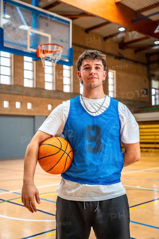 Young male basketball player holding ball in indoor court posing after training, looking confident and ready for the next game
