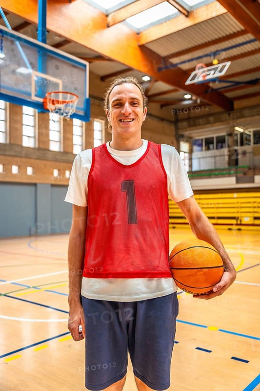 Smiling basketball player holding a ball while standing on an indoor court, exuding energy and readiness for the upcoming game