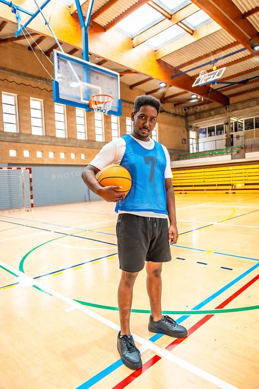 Young male basketball player holding a ball while standing confidently on an indoor court, showcasing athleticism and dedication to the sport