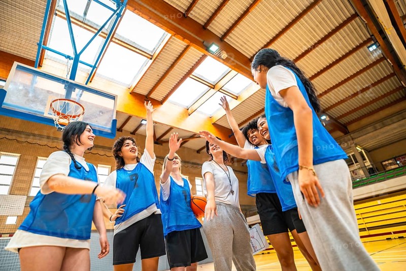 Basketball players and their coach celebrating a victorious moment with high fives in a vibrant gymnasium filled with energy and excitement