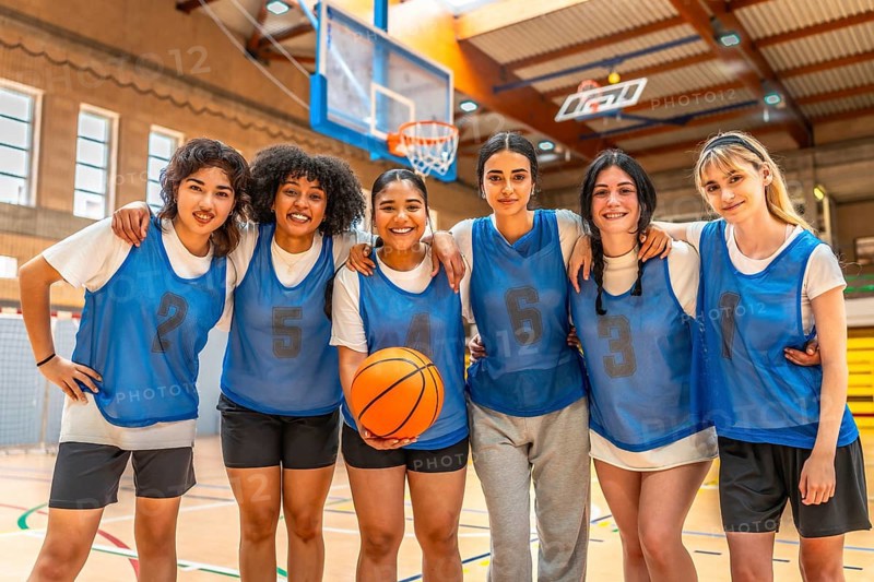 Diverse group of female basketball players hugging and holding ball, showcasing team unity and athletic spirit