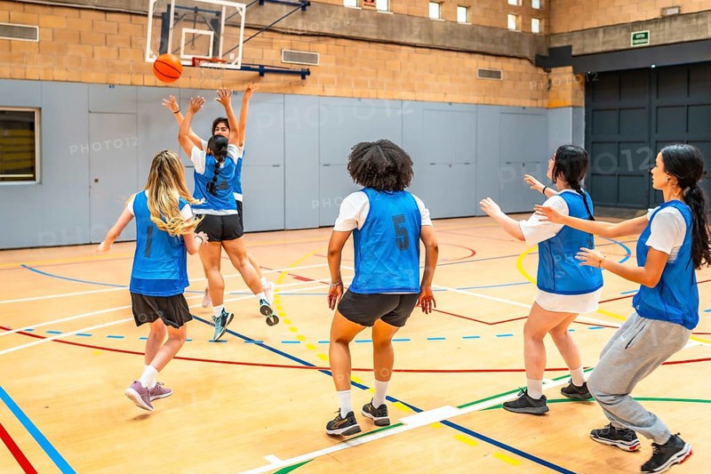 Group of young female athletes competing in a basketball match, showcasing their skills and teamwork in a vibrant sports hall environment