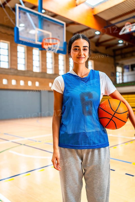 Young woman basketball player standing confidently on the court, holding a ball and embodying strength and determination in her sport