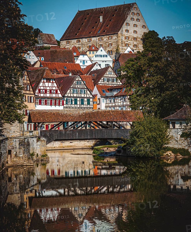 Half-timbered houses with red roofs are reflected in the river next to a wooden bridge in a picturesque medieval setting in the town of Schwäbisch Hall, Baden-Württemberg, Germany