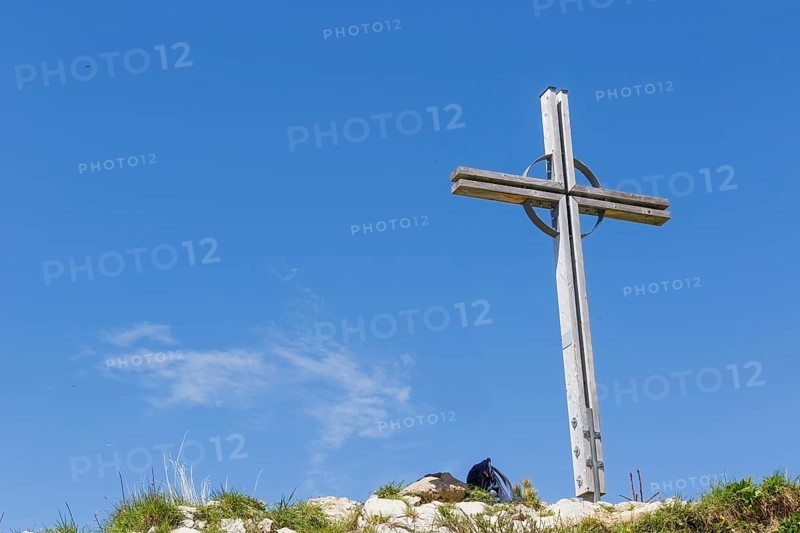 Summit cross of the Kuhgehrenspitze in Mittelberg rises in front of a bright blue sky in Kleinwalstertal, Mittelberg, Kleinwalsertal, Austria
