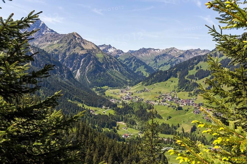 Alpine valleys with the villages of Mittelberg, Hirschegg and Riezlern amidst the surrounding mountains, framed by trees in Kleinwalsertal, Austria