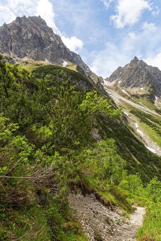 Stony path in an alpine mountain landscape under a blue sky with clouds and a view of the small and large Widderstein mountain peaks in Gemsteltal, Kleinwalsertal, Austria