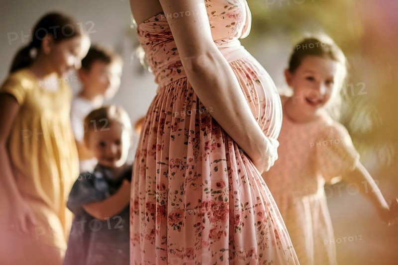 Woman with pregnant belly with happy children in blurry background, AI generated