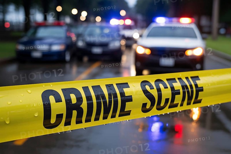 Bright yellow crime scene tape with water droplets stretches across a rainy street with police car in blurry background. Generative ai, AI generated