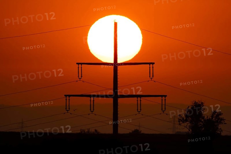 The sun rises behind an electricity pylon near Frankfurt am Main, Frankfurt am Main, Hesse, Germany