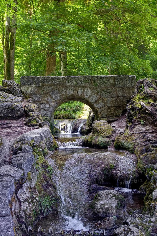 An old, small stone bridge over the Brühlbach, wild and romantic stream and source of the Urach waterfall in a dense forest, Bad Urach