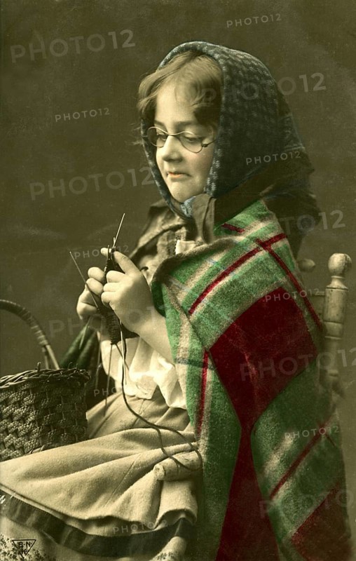 1920 Girl dressed as grandma knitting, girl with knitting needles and glasses in traditional dress knitting, historical photo