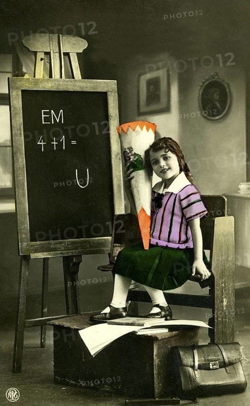 1920 A girl's first day at school, child with a sugar cone in front of a blackboard in a vintage scene, historical photo