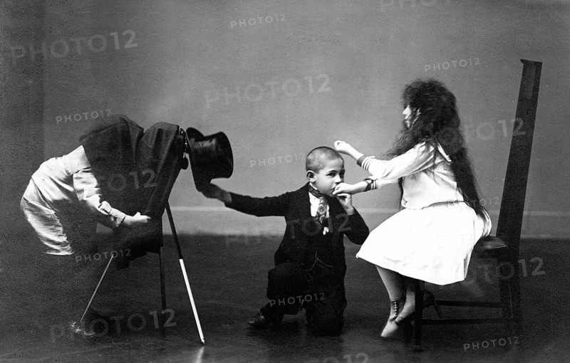 Children photograph hand kiss, 1920, A boy in suit and top hat playing with two other children, one child hanging upside down on a chair, historical photo