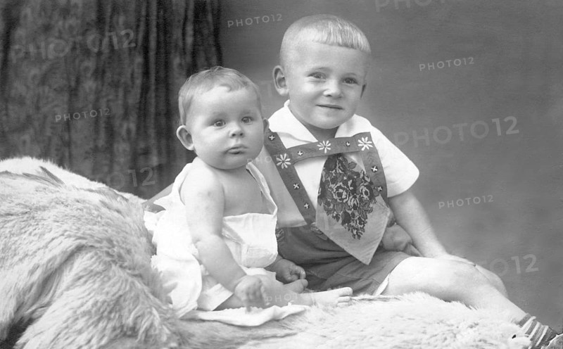 Two little boys on bed, 1930s, An older child holding a baby sitting on fur in a studio portrait, Historical photo