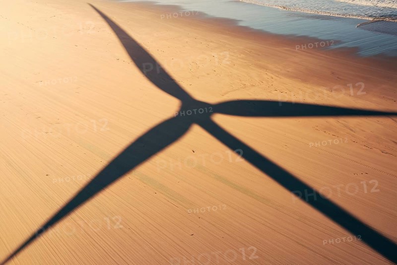 Wind turbine shadow on sunlit beach. A poetic symbol of clean energy blending with nature. generative ai, AI generated