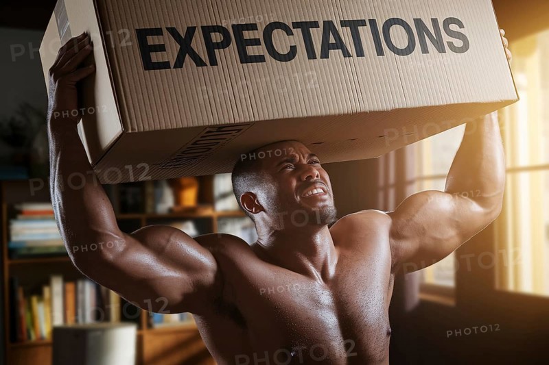 Man struggling to lift cardboard box labeled expectations in sunlit room, symbolizing male societal pressure and emotional burden. Generative AI, AI generated
