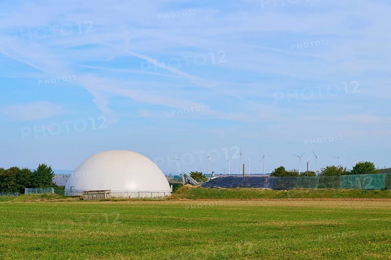 Biogas plant with wind turbines in the background, wide green field, Germany