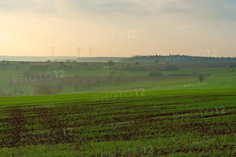 Wide green fields under a cloudy sky with wind turbines in the distance, Hornbach, Walldürn, Odenwald, Neckar-Odenwald Kreis, Baden-Württemberg, Germany