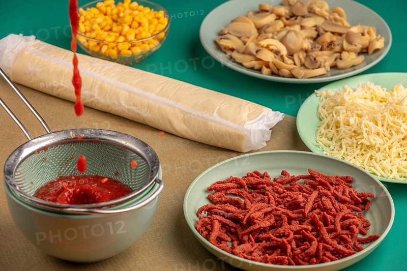 Tomato sauce drips into a sieve alongside other ingredients for pizza