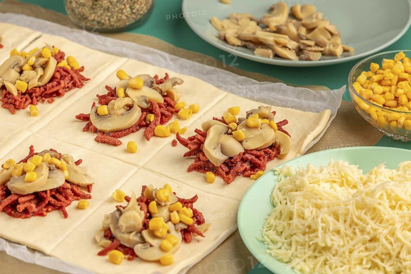 Sliced dough squares with tomato paste, bacon, mushrooms and sweetcorn alongside other ingredients for pizza, balls