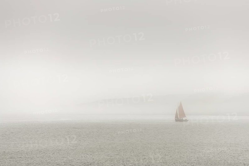 A sailing boat is travelling on the ocean on a cloudy day. The sky is overhanging and the water is calm. Camaret sur mer, Crozon, Finistere, Brittany, France
