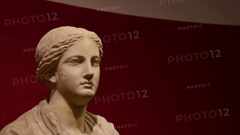 Ancient bust of a woman against a red background, showing classical stone carving, Archaeological Museum, Kos Town, Kos, Dodecanese, Greek Islands, Greece